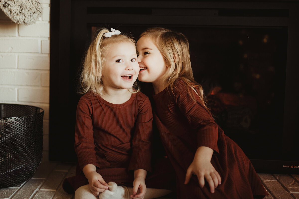 A big sister is telling her little sister a secret as they giggle.