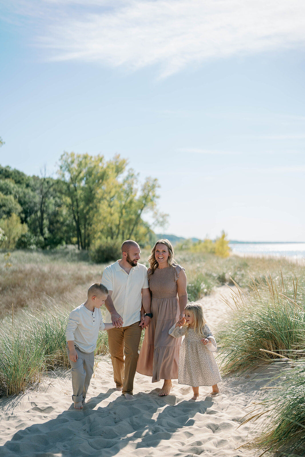 A family holding hands walking through the tall grass of the dunes at Weko Beach together during a family session 