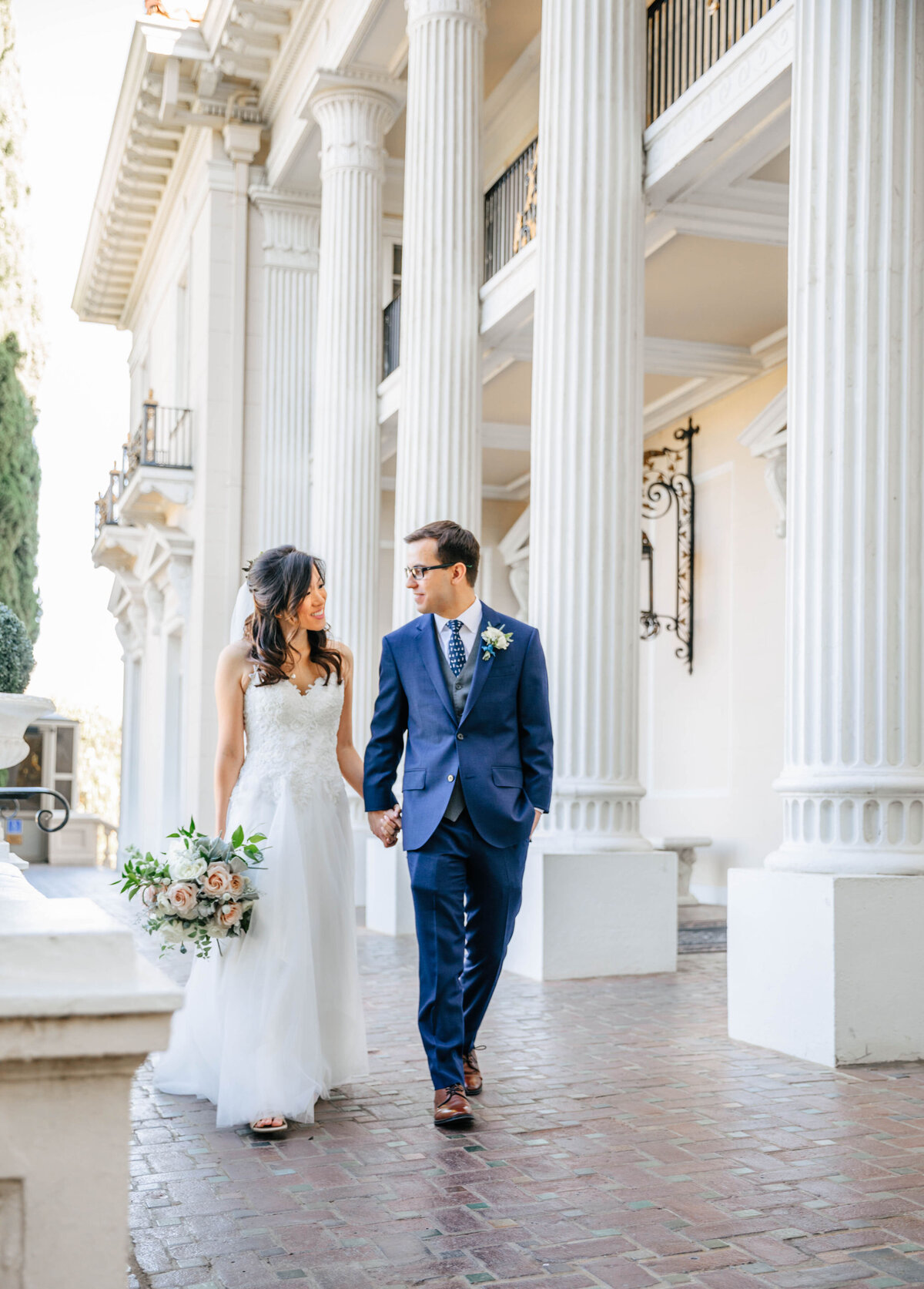 bride and groom walking in front of columns