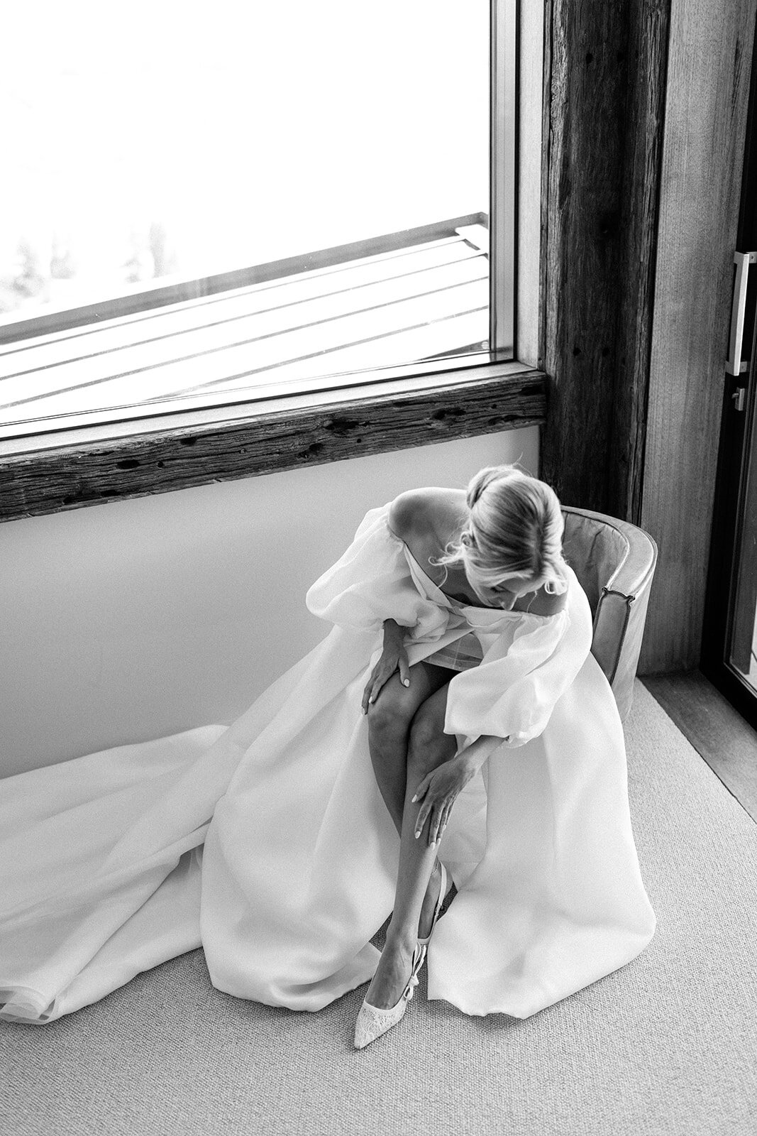 black and white image of bride putting on wedding shoes 