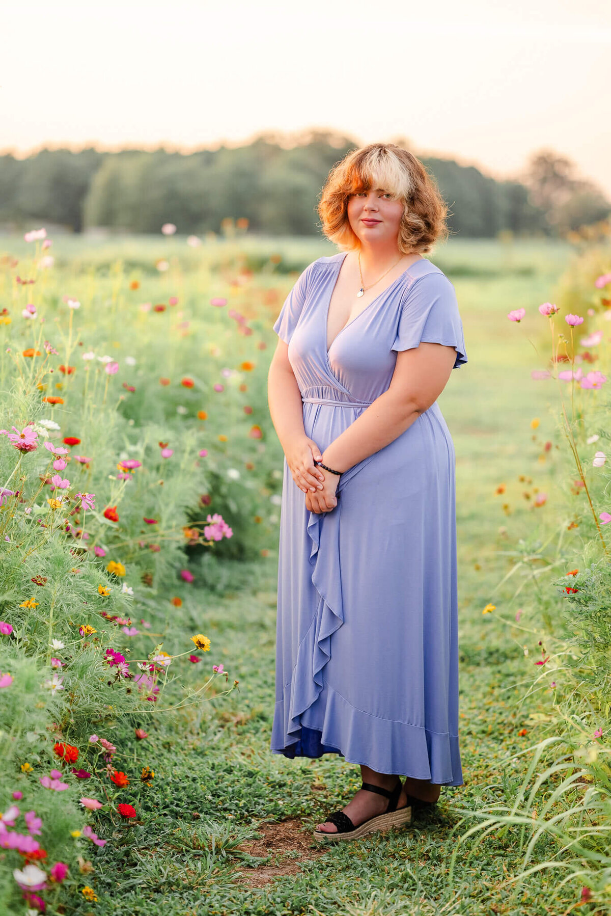 A high school senior, wearing a light purple, ruffle dress, stands in a field of colorful flowers.