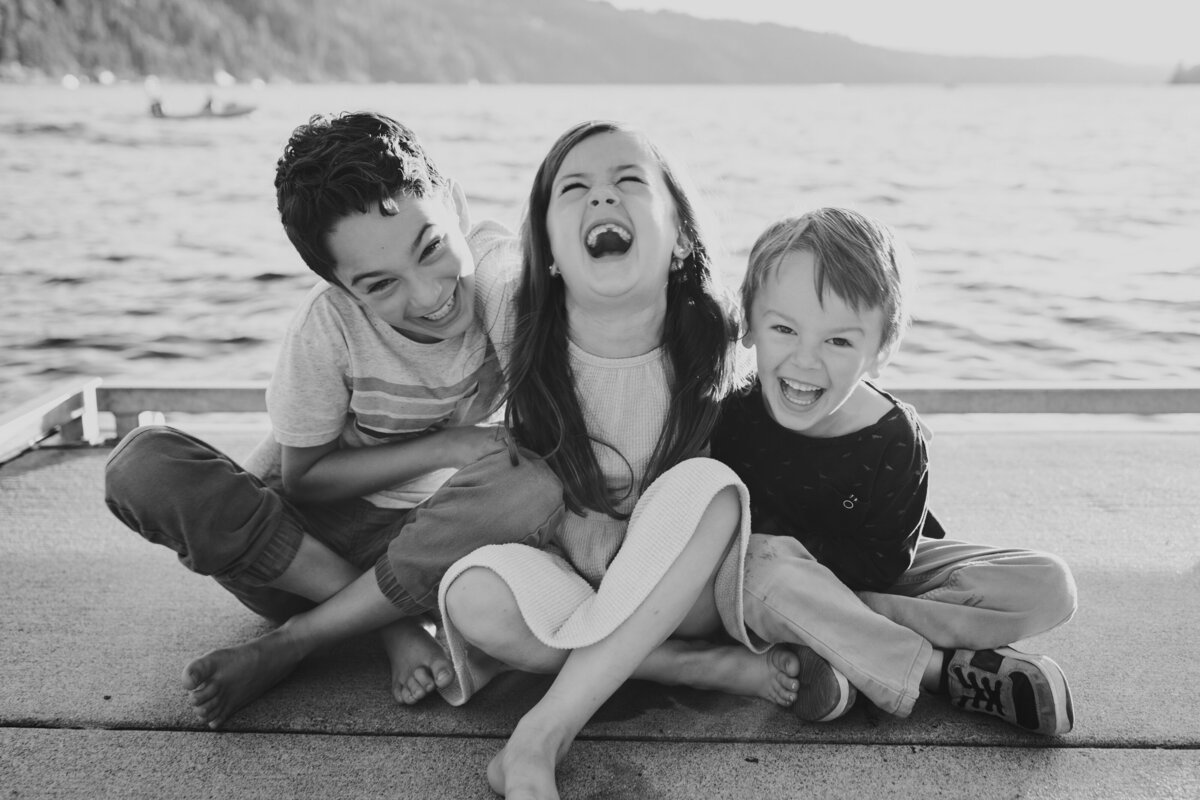Three young siblings  laugh together at the end of dock on Coeur d'Alene Lake.