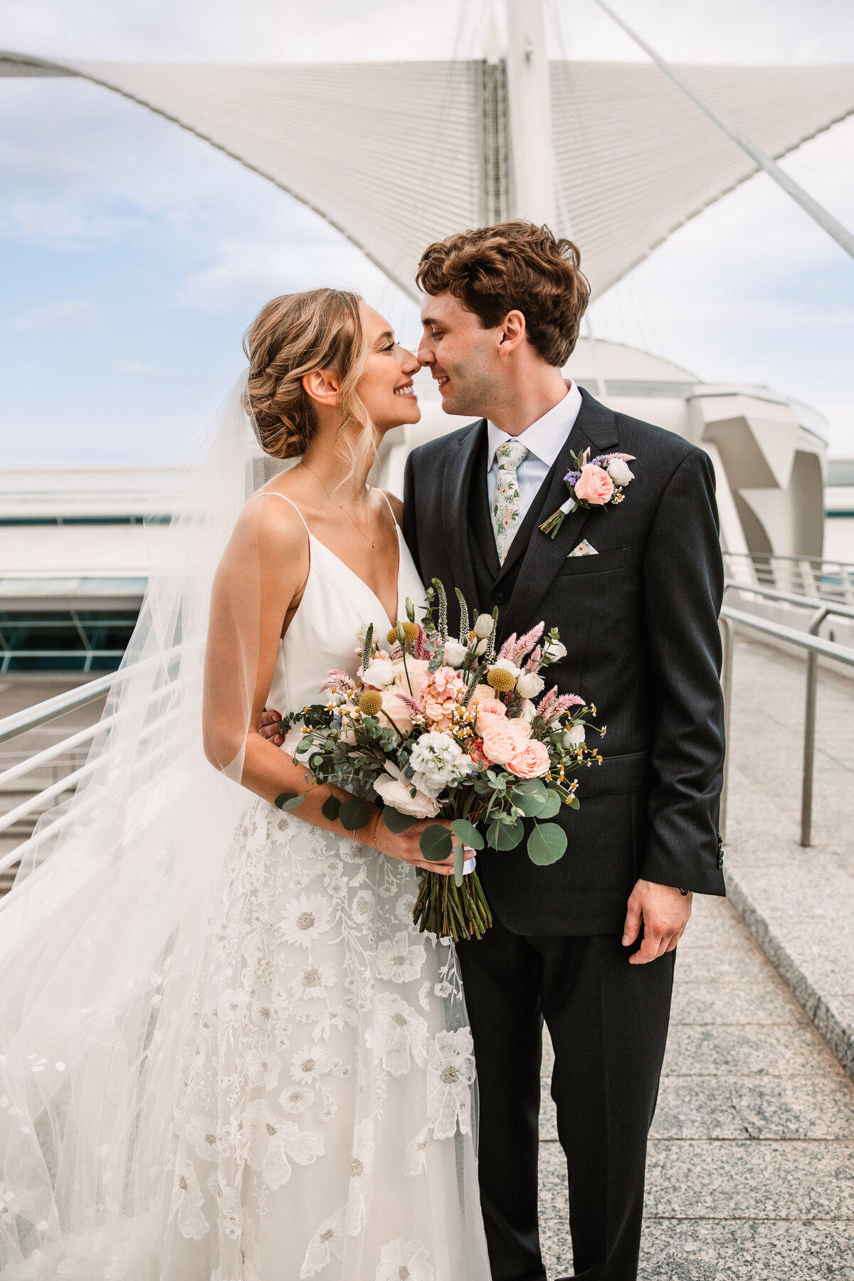 Newlyweds eskimo kiss while on a skyway while holding the bouquet
