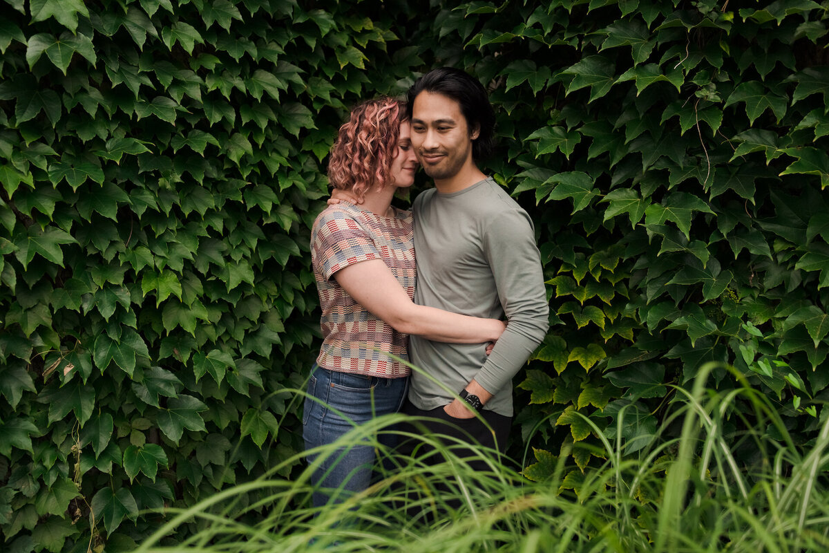 A couple embrace in front of green Ivy