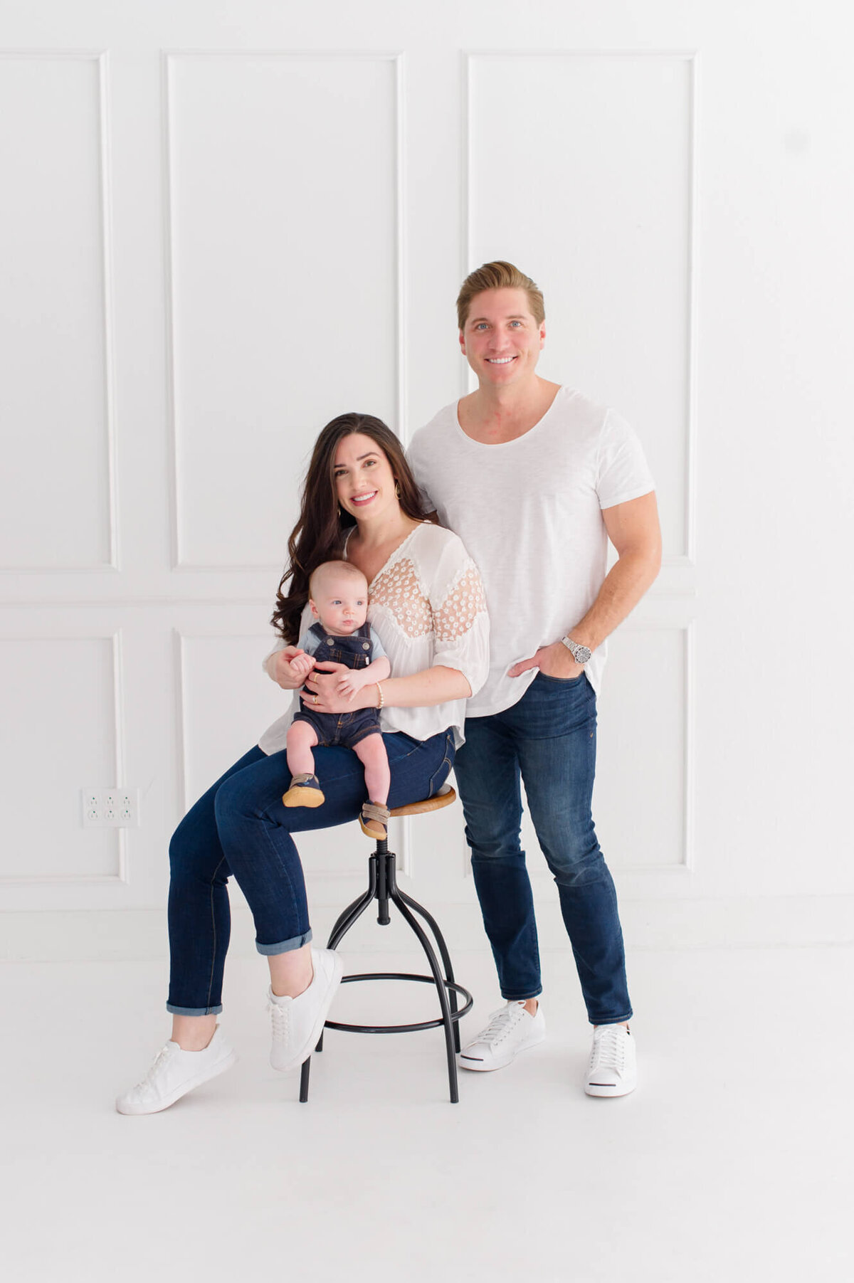 Parents and newborn baby smile at the camera in  an all white natural light studio in Orlando