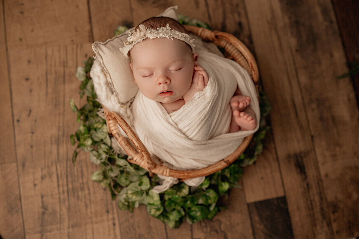 newborn baby girl wrapped up and posed in a bamboo basket during newborn photography shoot