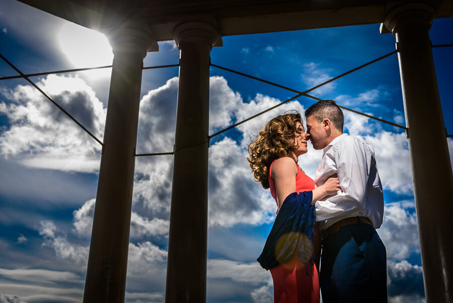 A couple embraces surrounded by pillars with a blue sky backdrop