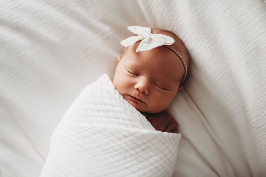 newborn swaddled by photographeron bed
