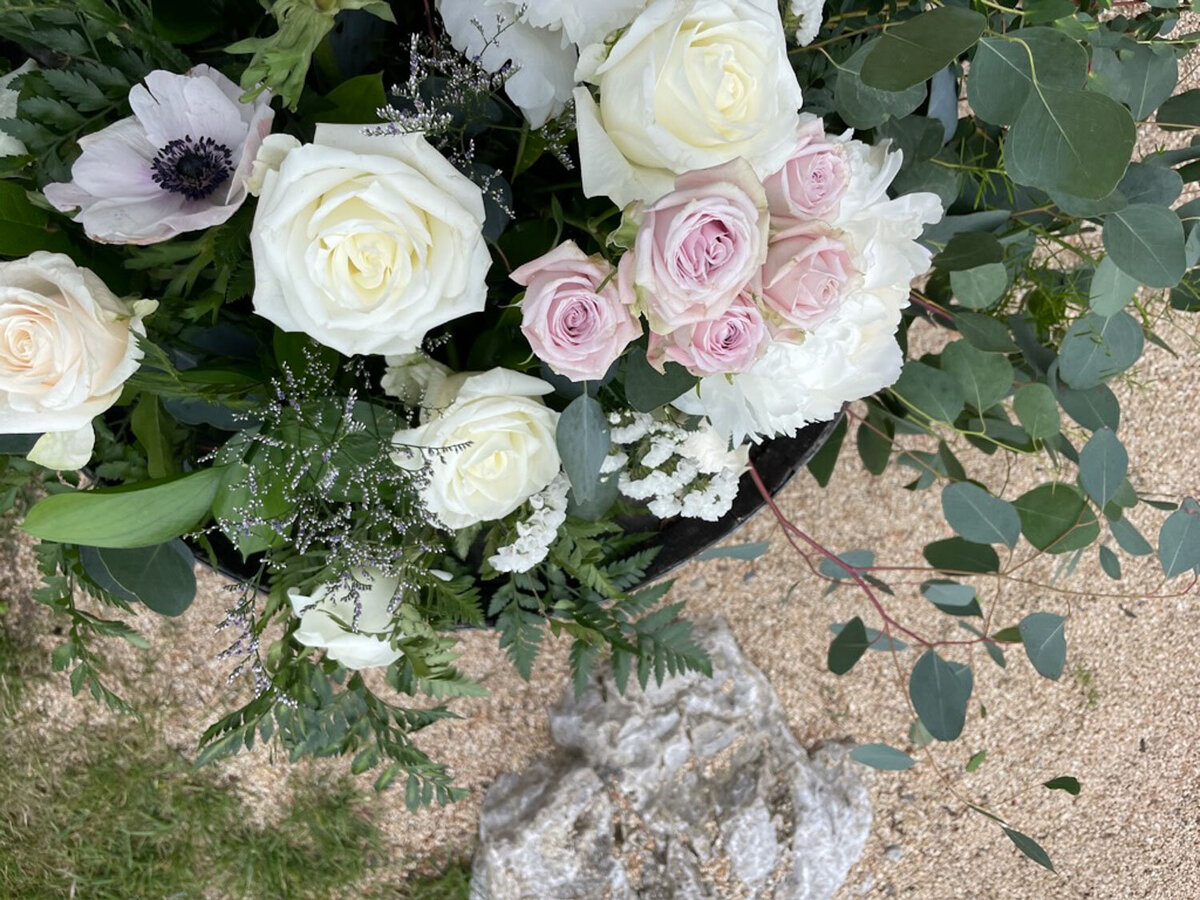 Close-up of a white and pink floral arrangement with greenery on gravel