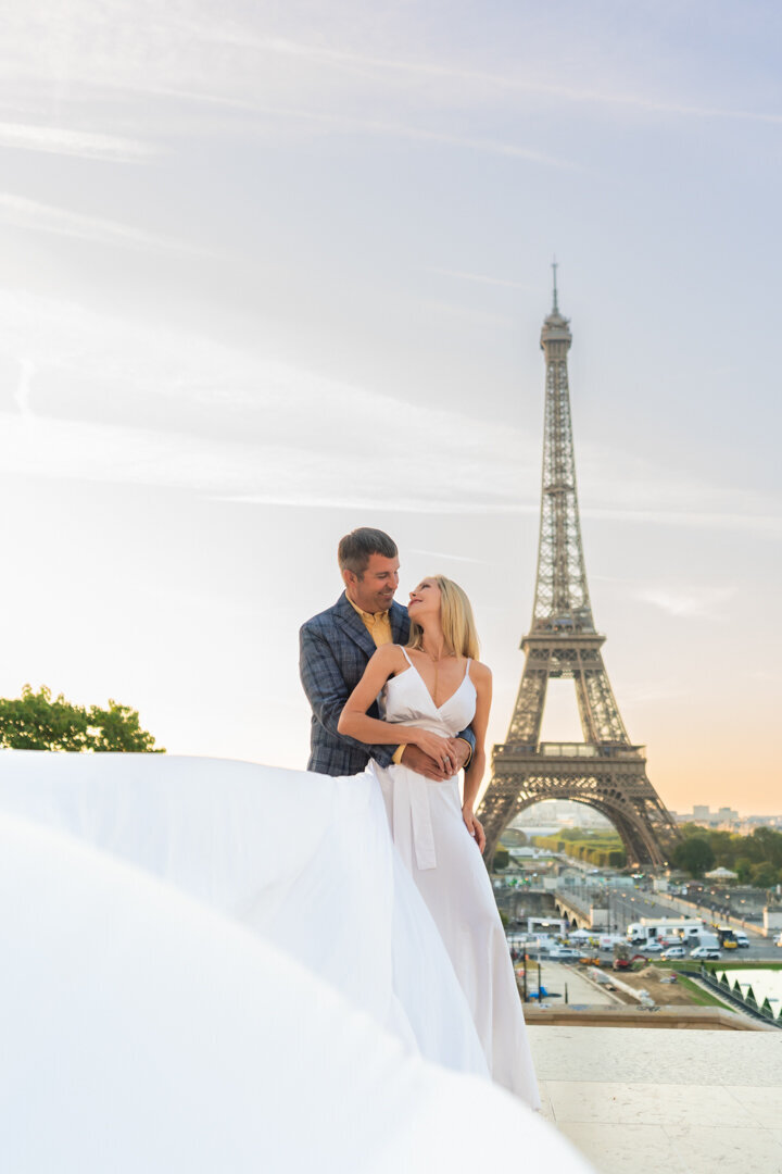 Sunrise Eiffel Tower couple embrace, white flying dress photoshoot Paris, golden morning light photography