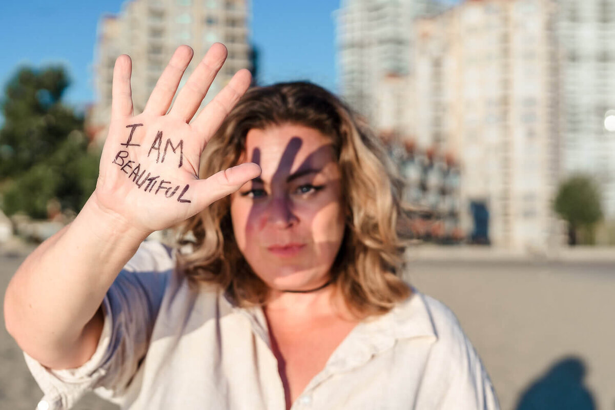 woman holding hand towards the camera with the words I am beautiful written on it