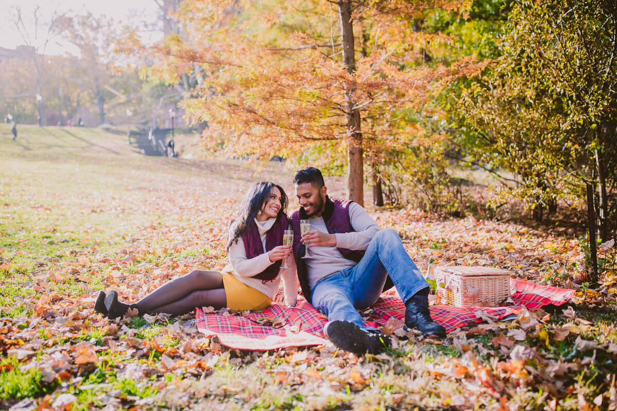 A couple having a picnic during their engagement session in the middle of the fall at central park nyc
