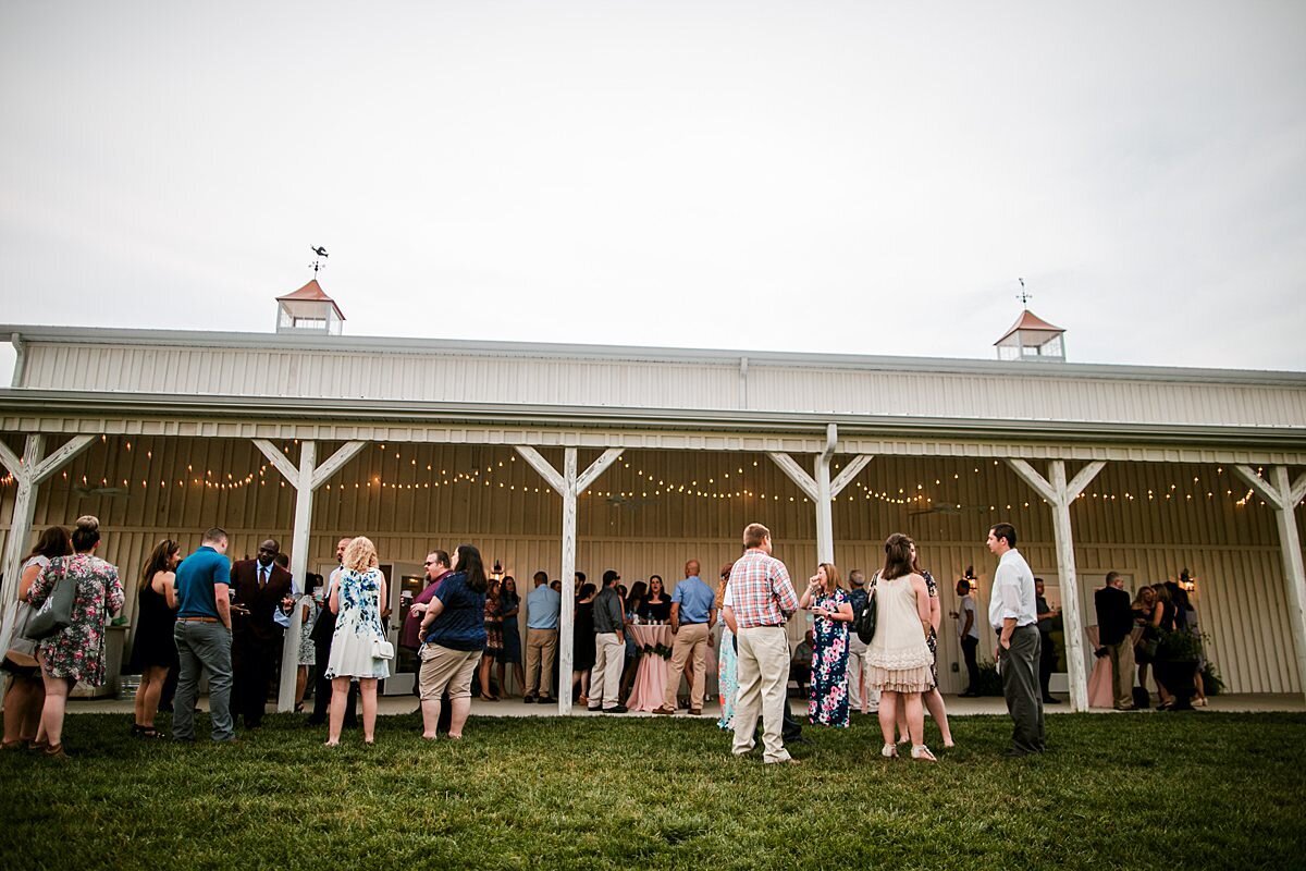 Long white wedding barn porch with cocktail tables set up for a cocktail hour reception at White Dove Barn. Guests enjoy wedding cocktails.