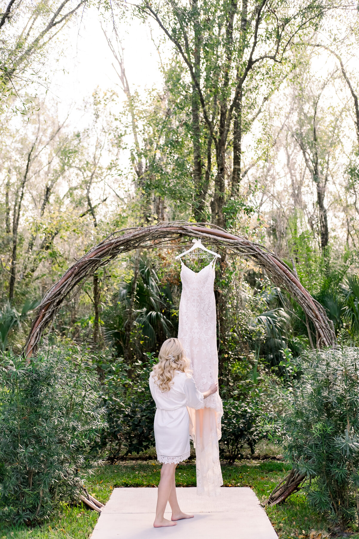 Bride adjusting her wedding dress on the hanger under a woven tree branch arch in Sarasota, FL