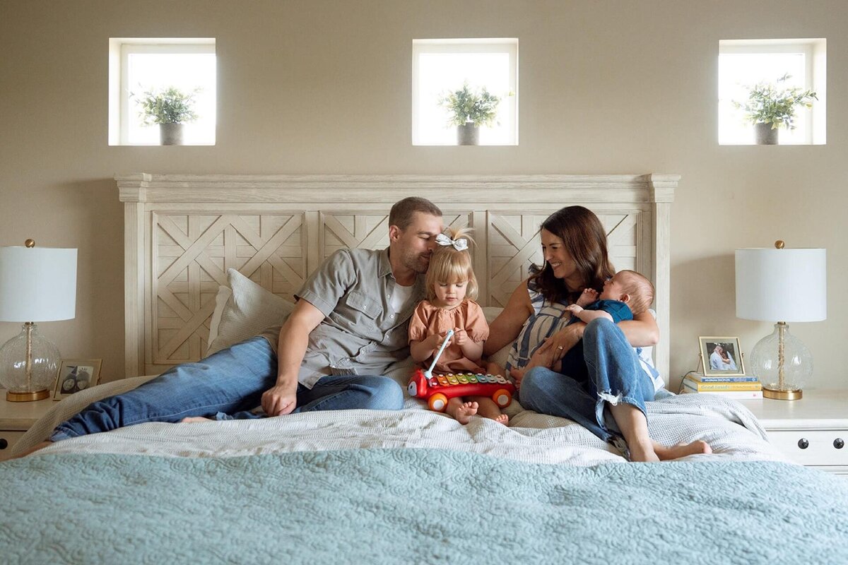 colorful family in bed at home with newborn baby
