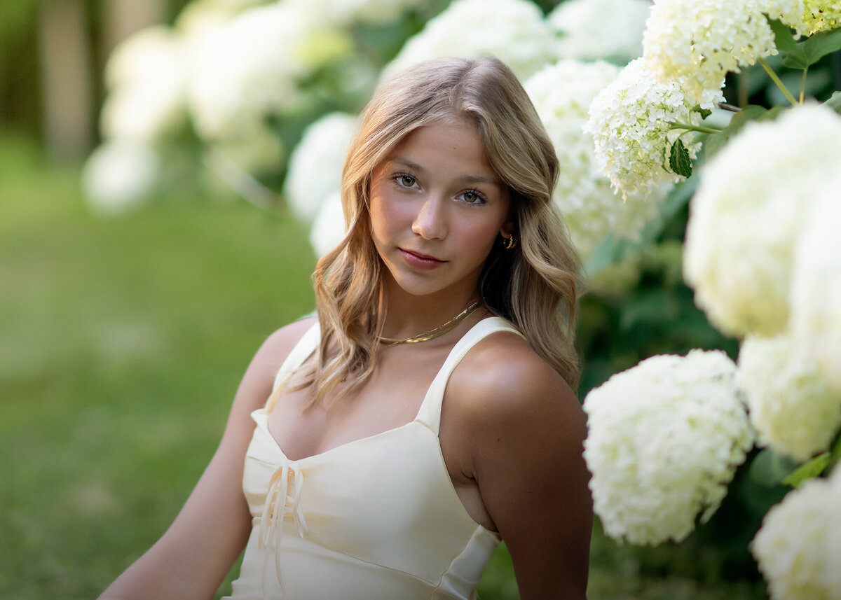 A teenage girl wearing a yellow dress sits next to white flowers