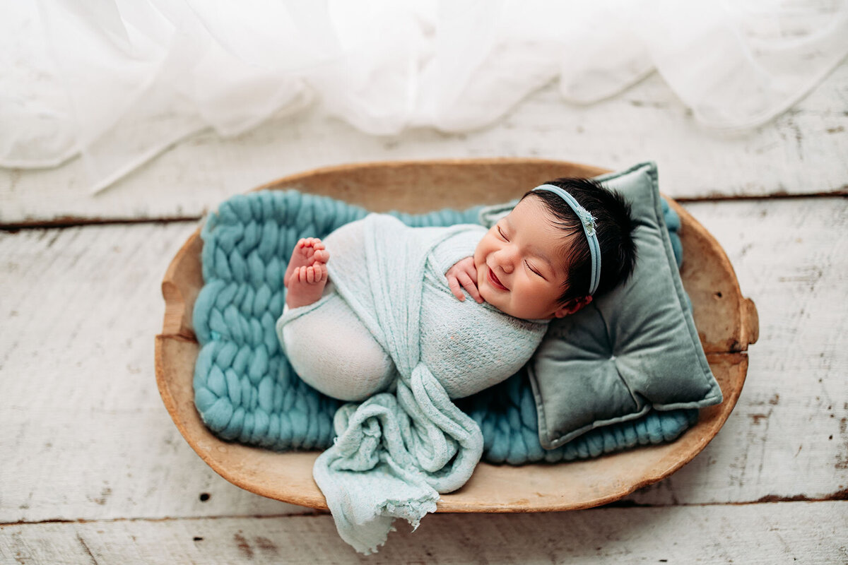 Newborn baby with lots of dark hair smiles in antique bowl as she is photographed for her newborn session in Jen Howell Photography's white studio in Germantown, TN.