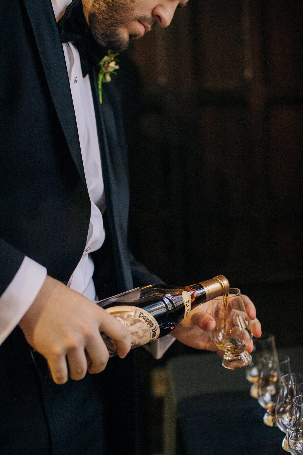 Man pouring bourbon into shot glasses for his groomsmen