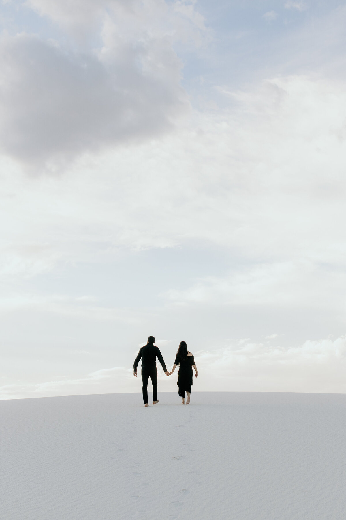 man and woman holding hands walking together at white sands NP