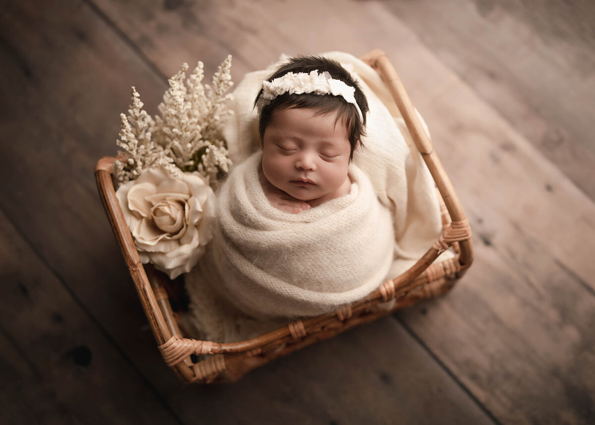 Aerial image. Baby girl is swaddled in a cream wrap with a cream floral headband. Baby is sleeping. Captured by best Lake Elsinore newborn photographer Bonny Lynn Photography