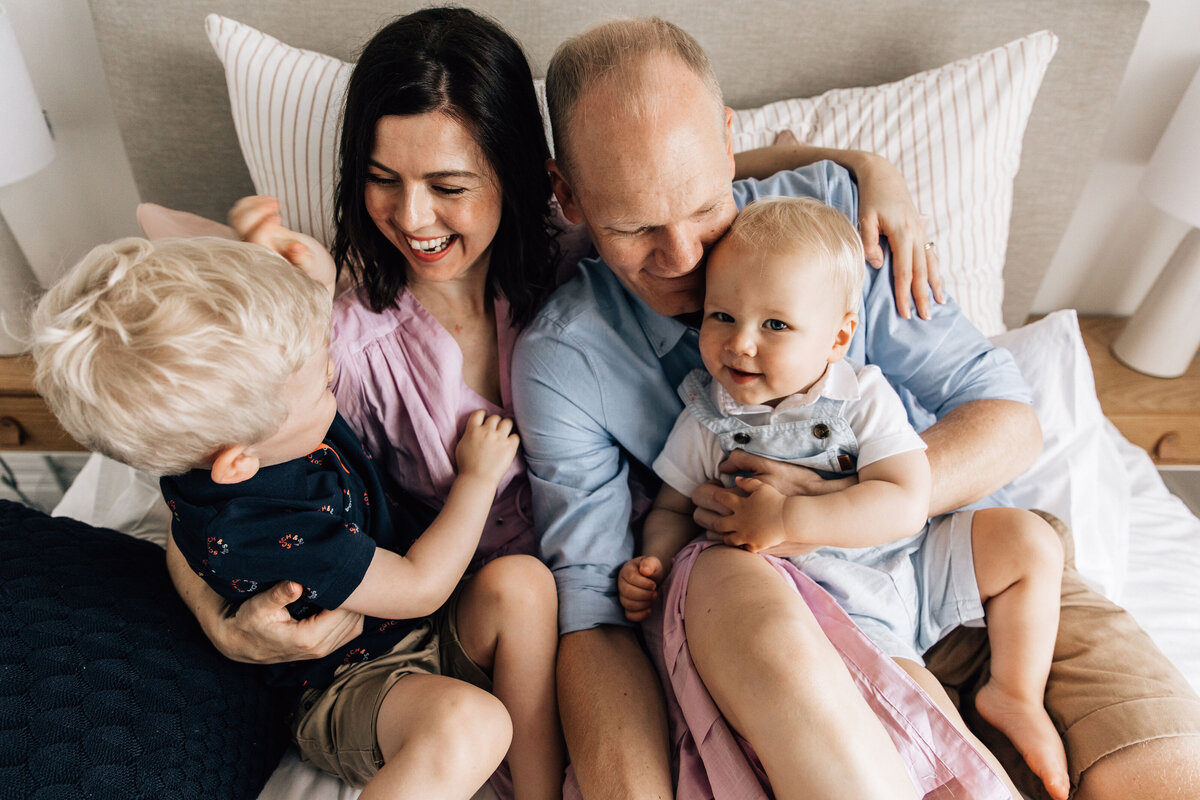 Mother, father and 2 young boys cuddle on bed