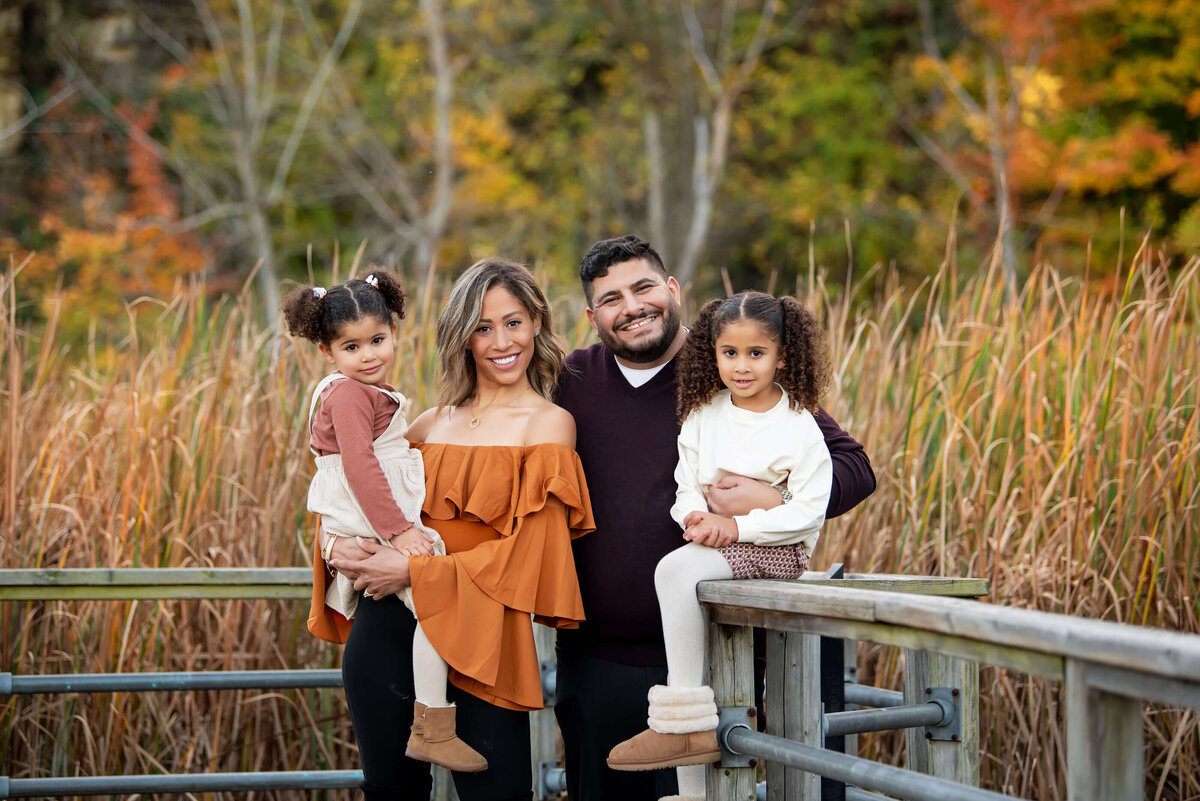 Mom and dad with their daughter on a wood bridge in the fall for their Burlington, family photographer session