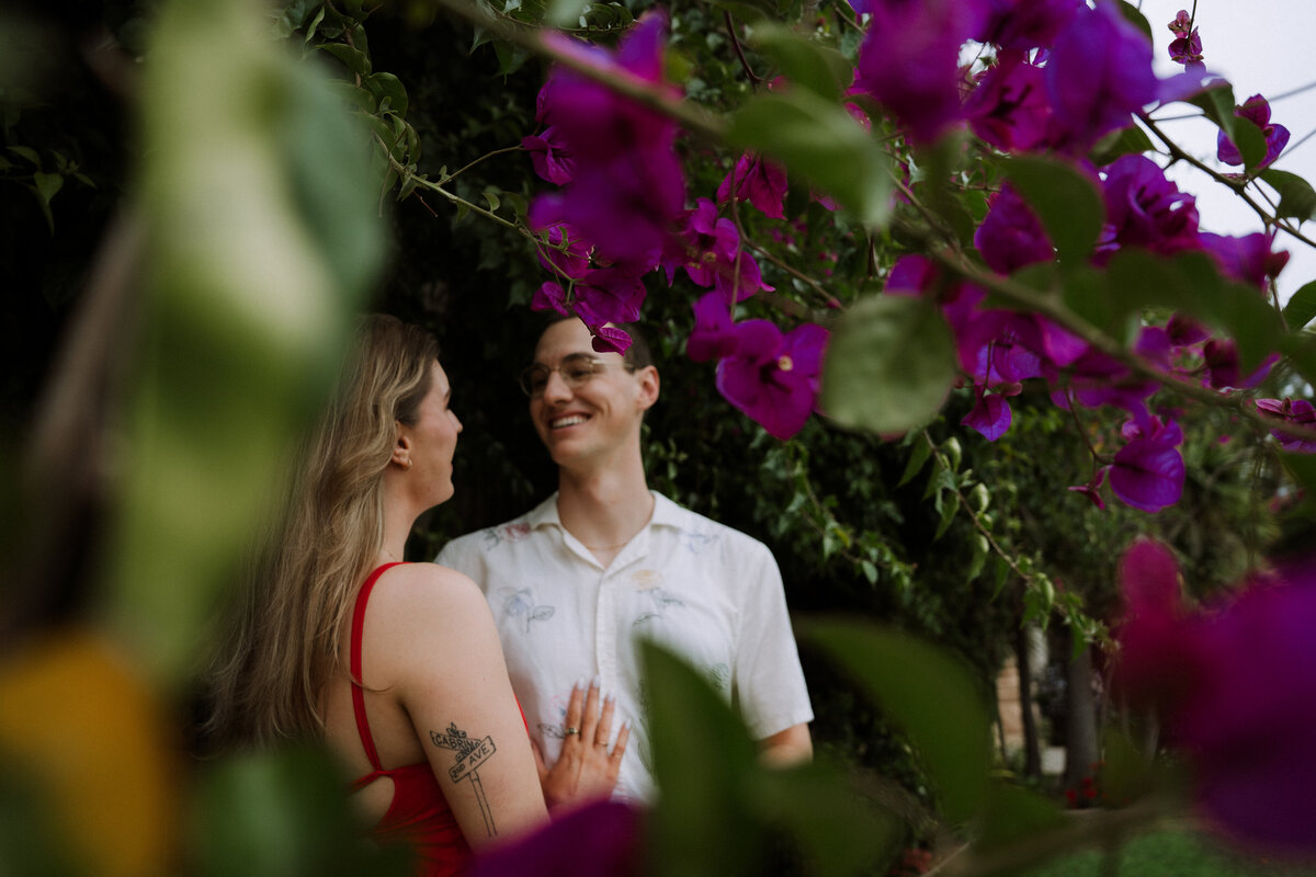 happy couple smiling at each other, candid photography behind flowers