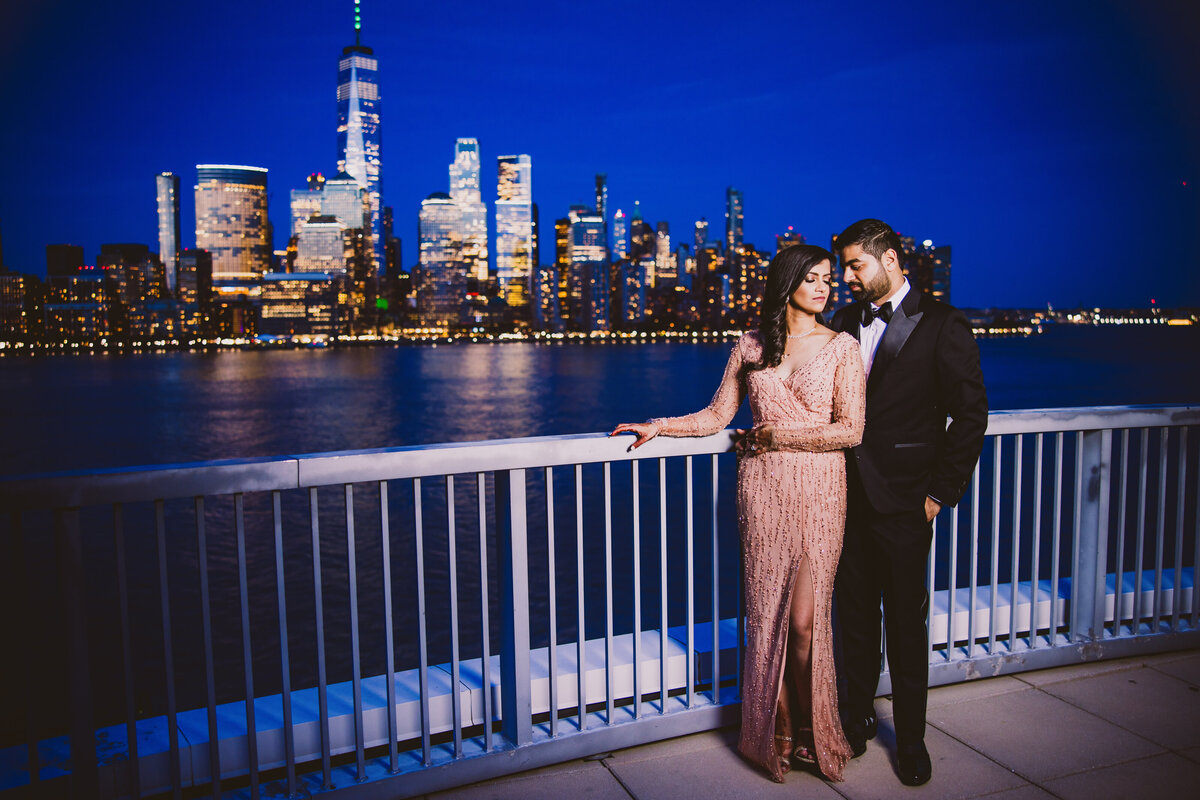 A bride and groom having a moment at the balcony outside the jersey city hyatt overlooking the nyc skyline lit up at night
