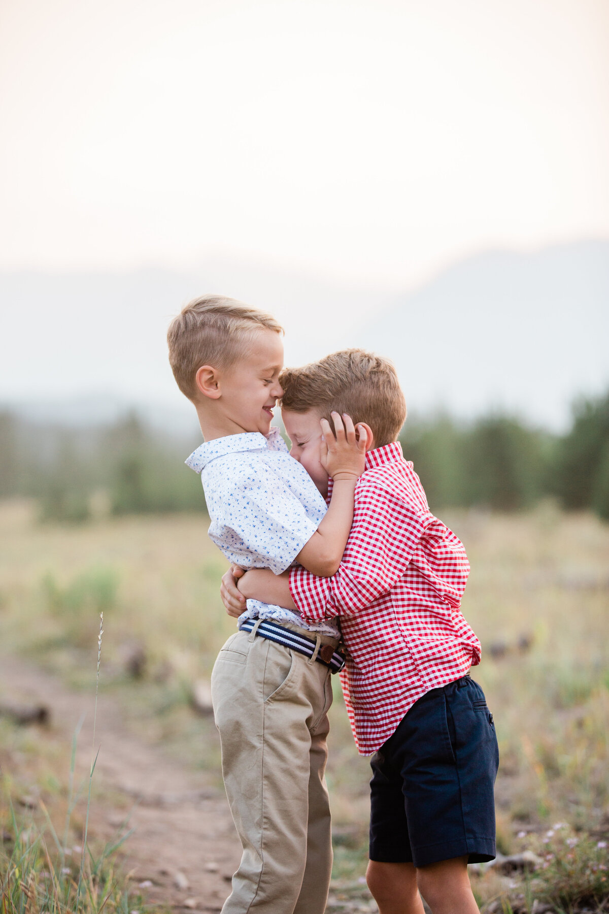 Two young brother are hugging tightly and laughing. They are in a grassy mountain field