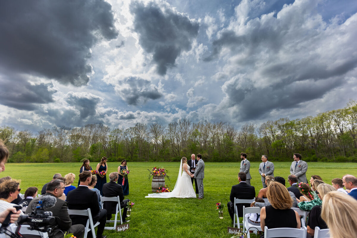 Outdoor wedding ceremony with guests seated under a dramatic sky.