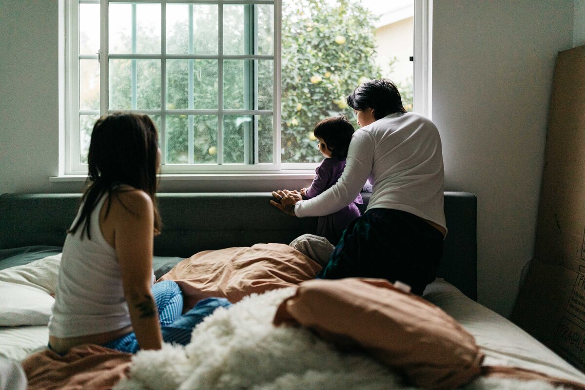 Mother is looking at her husband and toddler baby playing on the bed. 