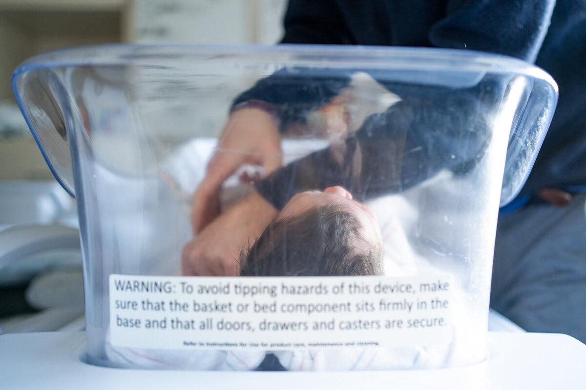 Looking through clear bassinet at the baby while Dad swaddles tight
