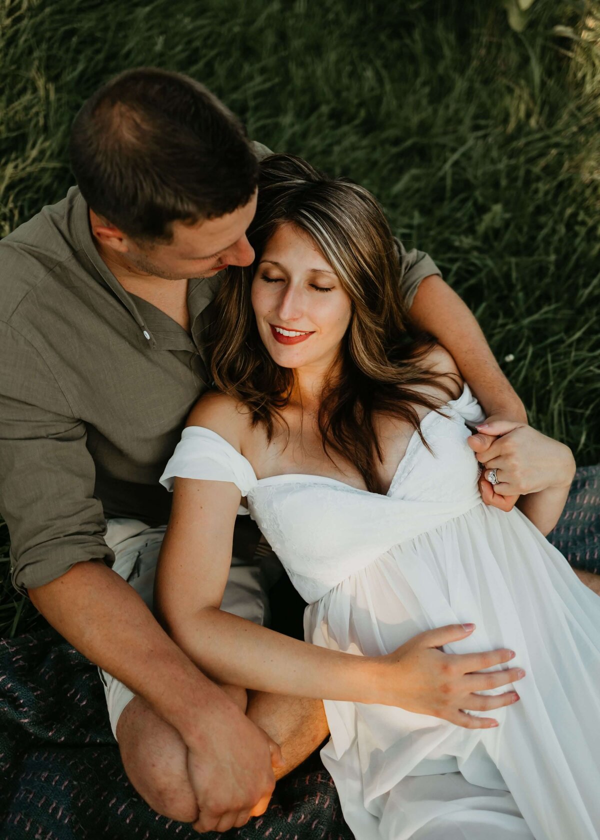 A couple expecting a baby, peacefully lounging on a blanket in a grassy field as captured by a Pittsburgh maternity photographer.