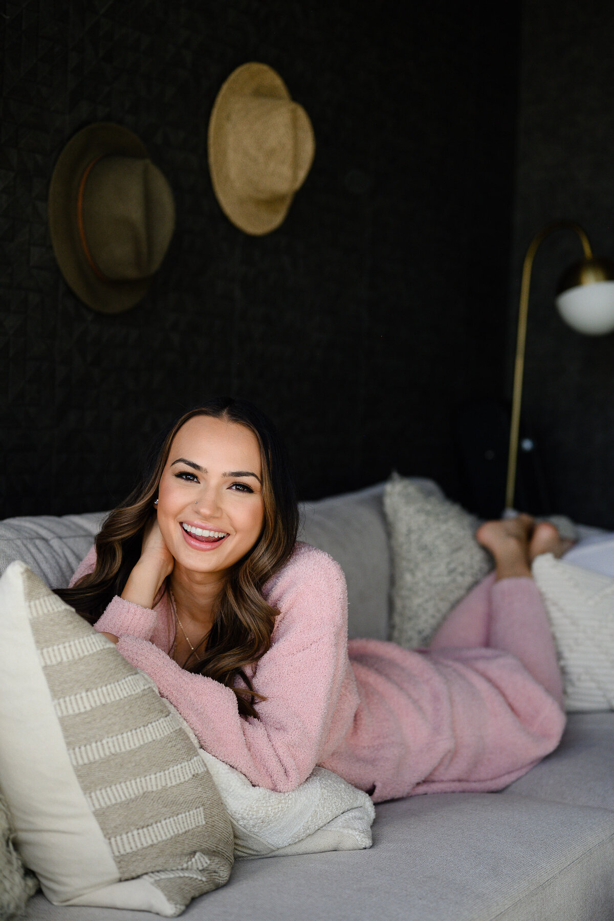 branding photos with woman in a pink matching set laying on a couch and smiling as she poses with Denver commercial photographers