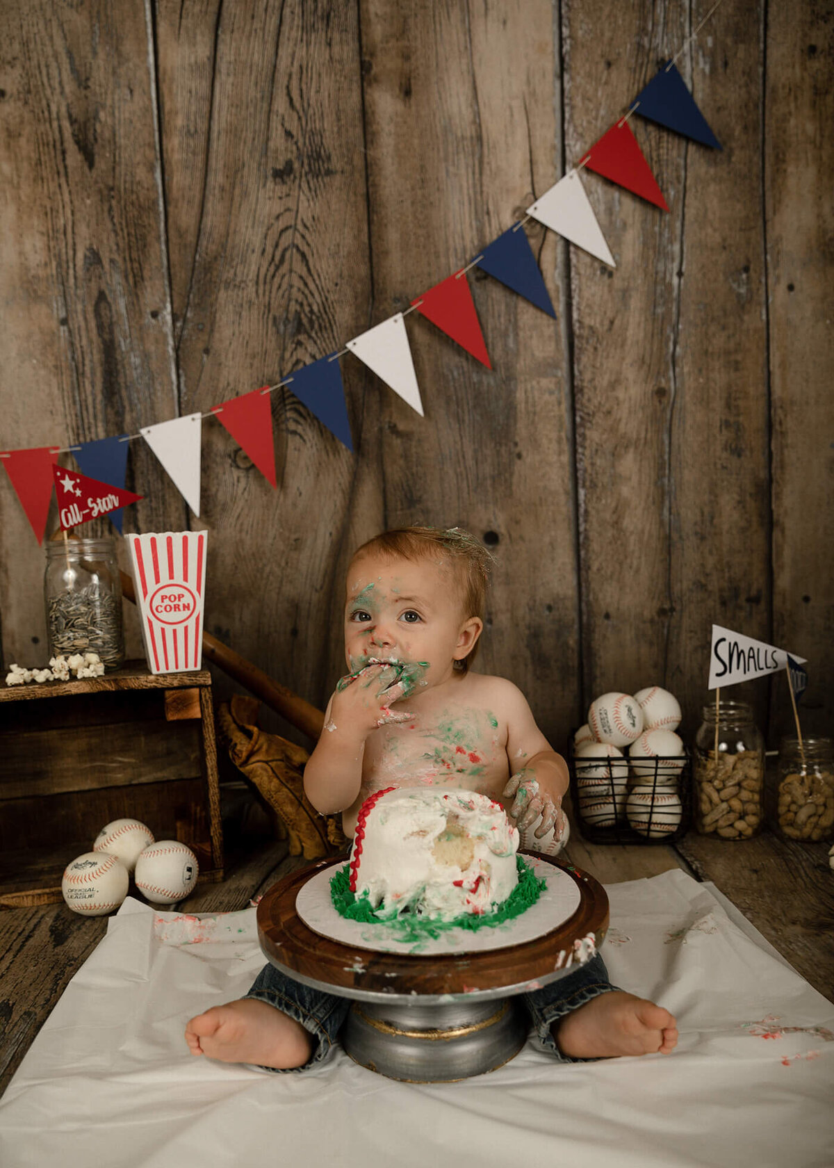 1 year old boy eating his baseball cake. Baseball themed decorations in the background.
