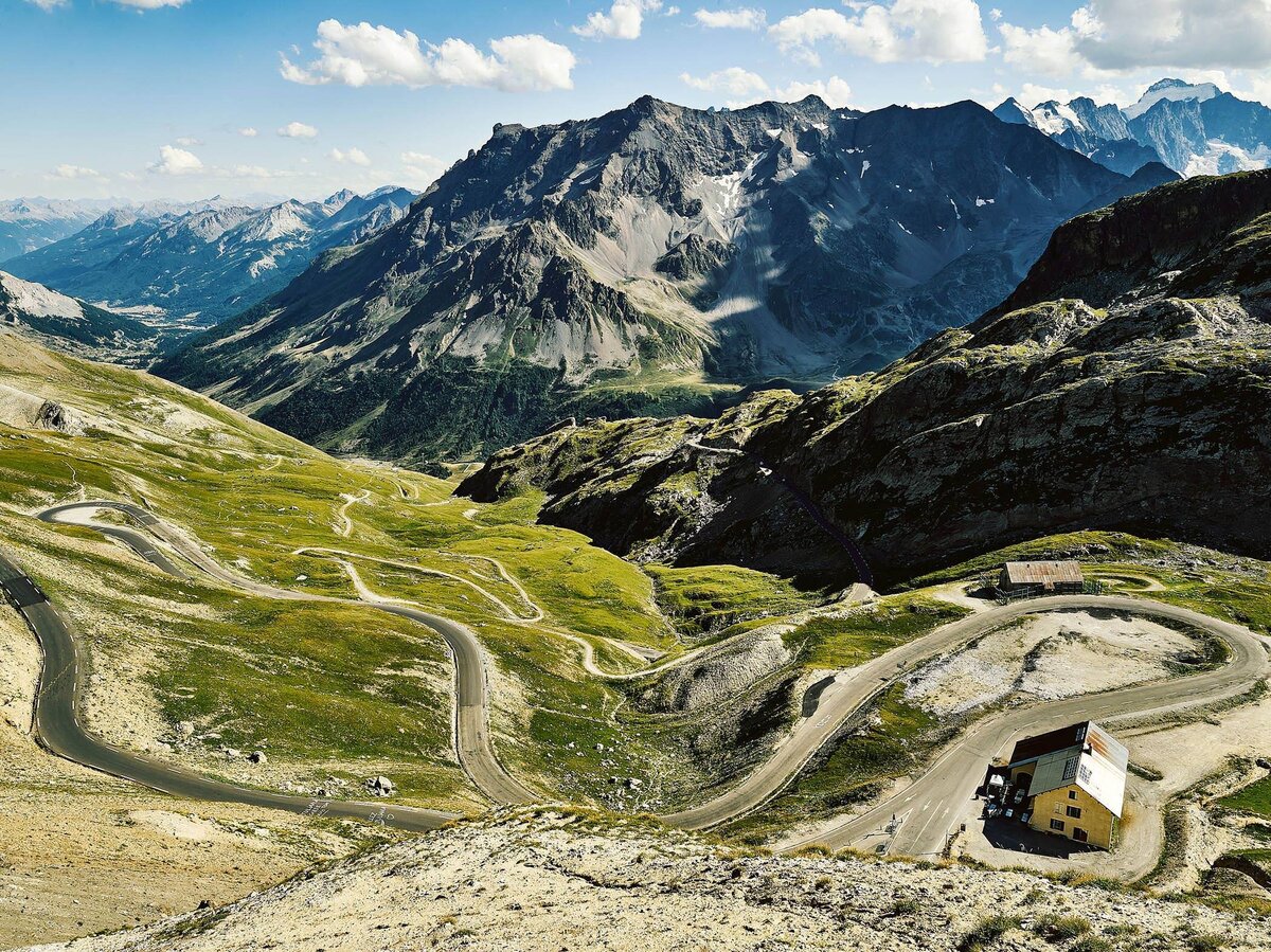 Panoramablick auf eine kurvige Alpenstraße inmitten beeindruckender Hochgebirgslandschaft – professionelle Landschaftsfotografie für Werbung und Editorials