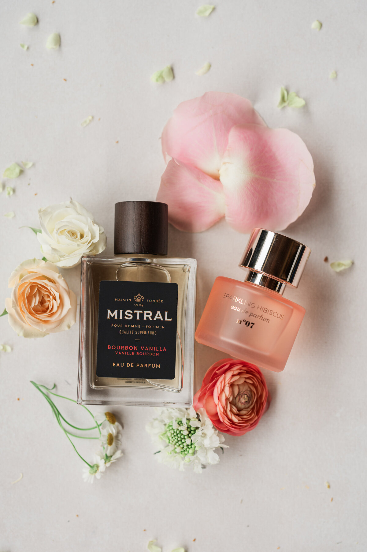 Two perfume bottles with flowers laid around them