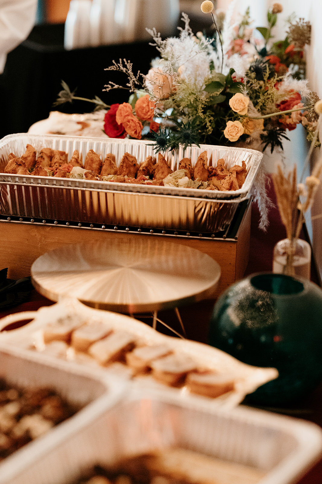 Table setting with trays of food and floral decor, capturing a cozy and inviting reception ambiance.