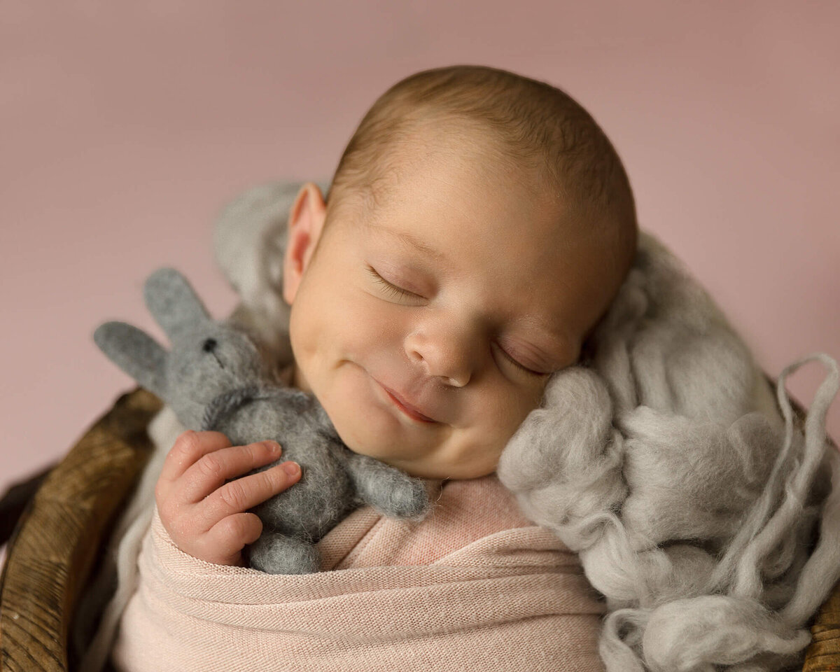 Newborn girl cuddling a gray bunny as she sleeps.