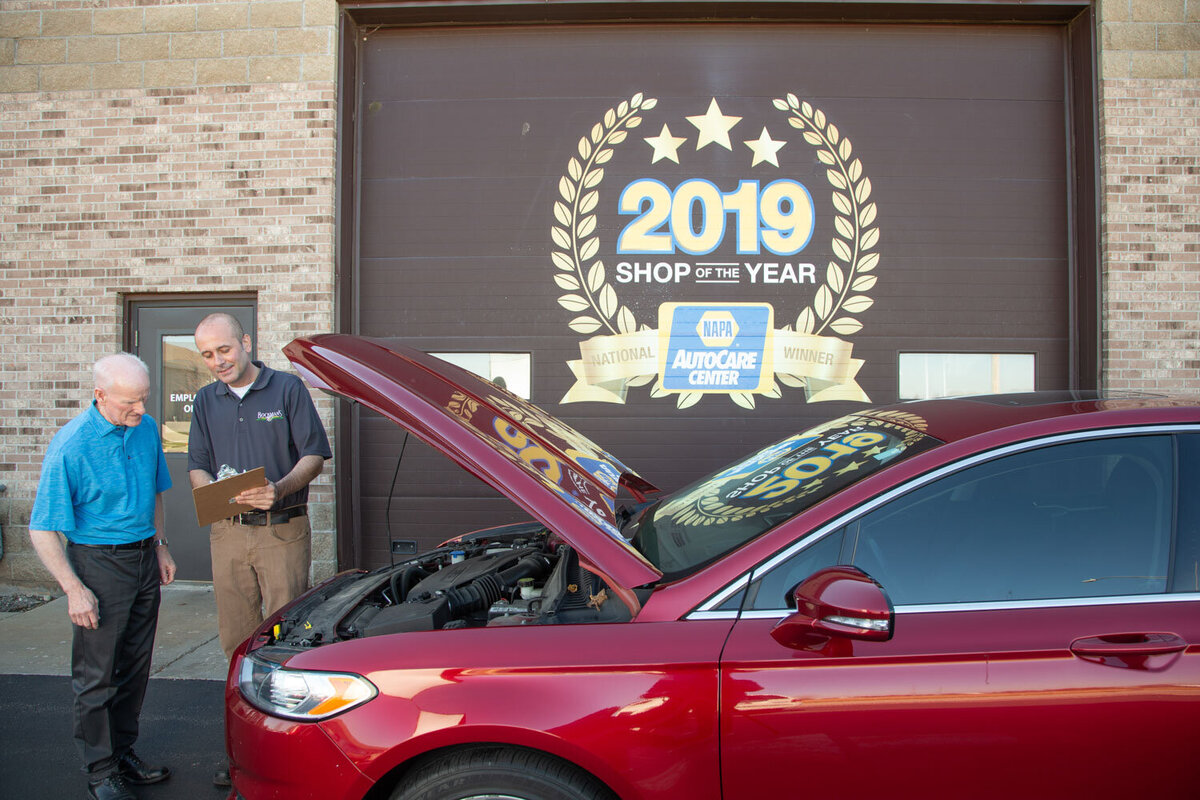A red car is parked in front of a sign that says 2019 shop of the year