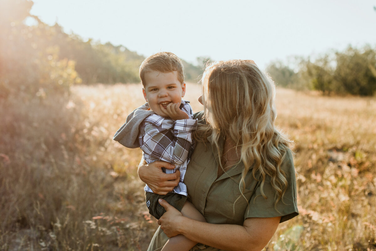 Mother hugs her son, holding him on her hip as he giggles joyfully.
