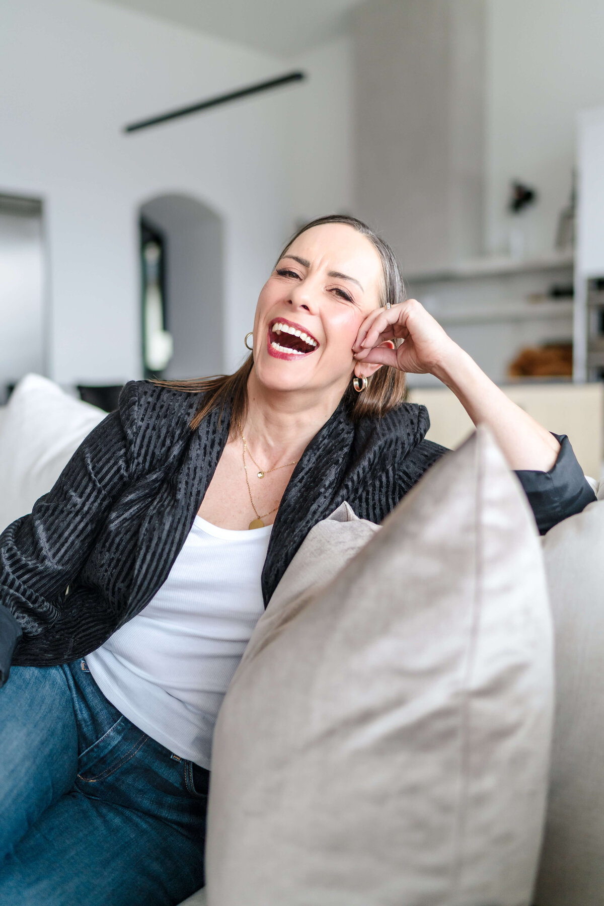 laughing woman in striped black blazer sitting on beige couch laughing at camera