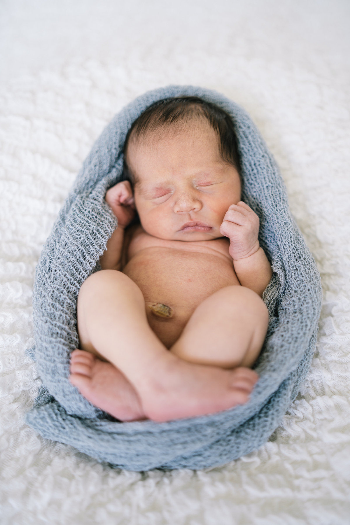 Newborn wrapped in cloth and laying on white blanket in a San Antonio Photography studio.