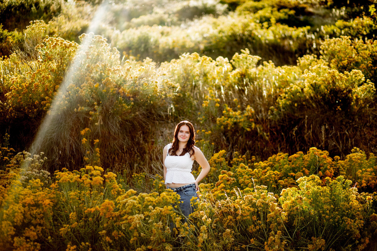girl in white tank top stands in middle of yellow flowers