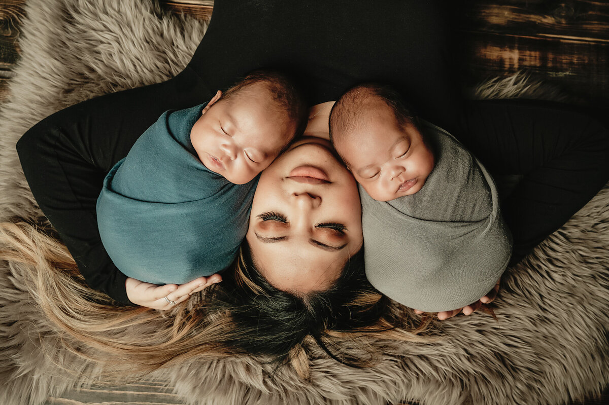 Mom laying on her back craddling her twins on each arm at their studio  portraits.