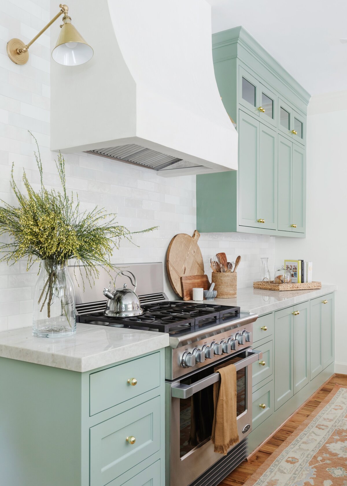 oyster creek studios oak forest remodel light green kitchen cabinets with white walls and stainless steel oven with runner rug in kitchen