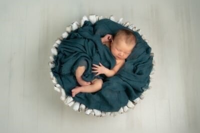 Professional newborn portrait by St Augustine family photographers showing peaceful sleeping baby wrapped in teal blanket in white bowl
