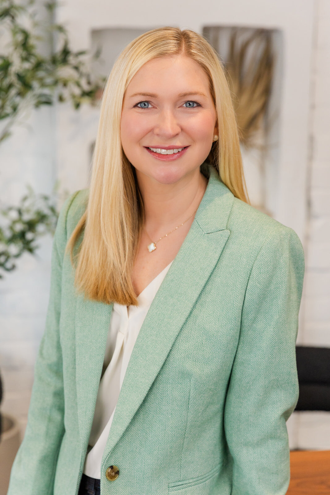 woman wearing a white blouse an a light green jacket sitting on the edge of a desk during portraits session