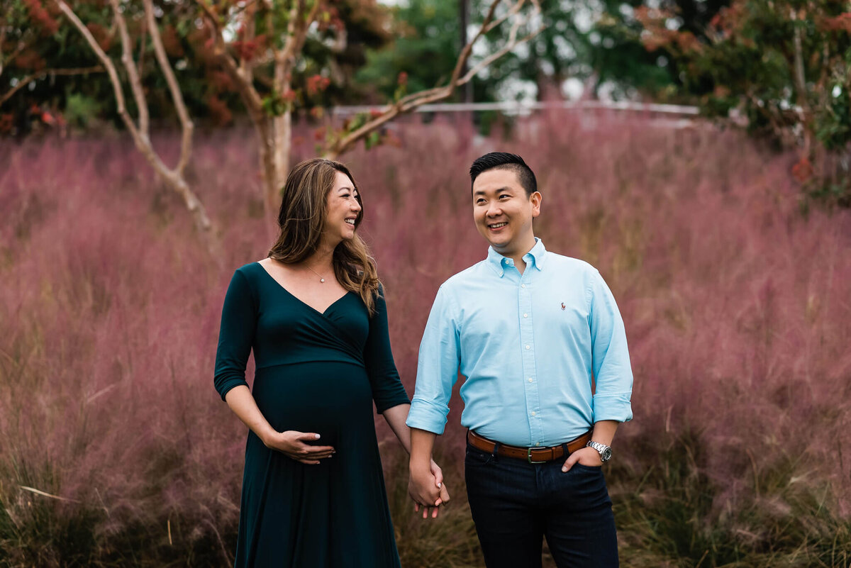 Expecting woman laughs at something man said while holding hands, captured by a Northern Virginia maternity photographer