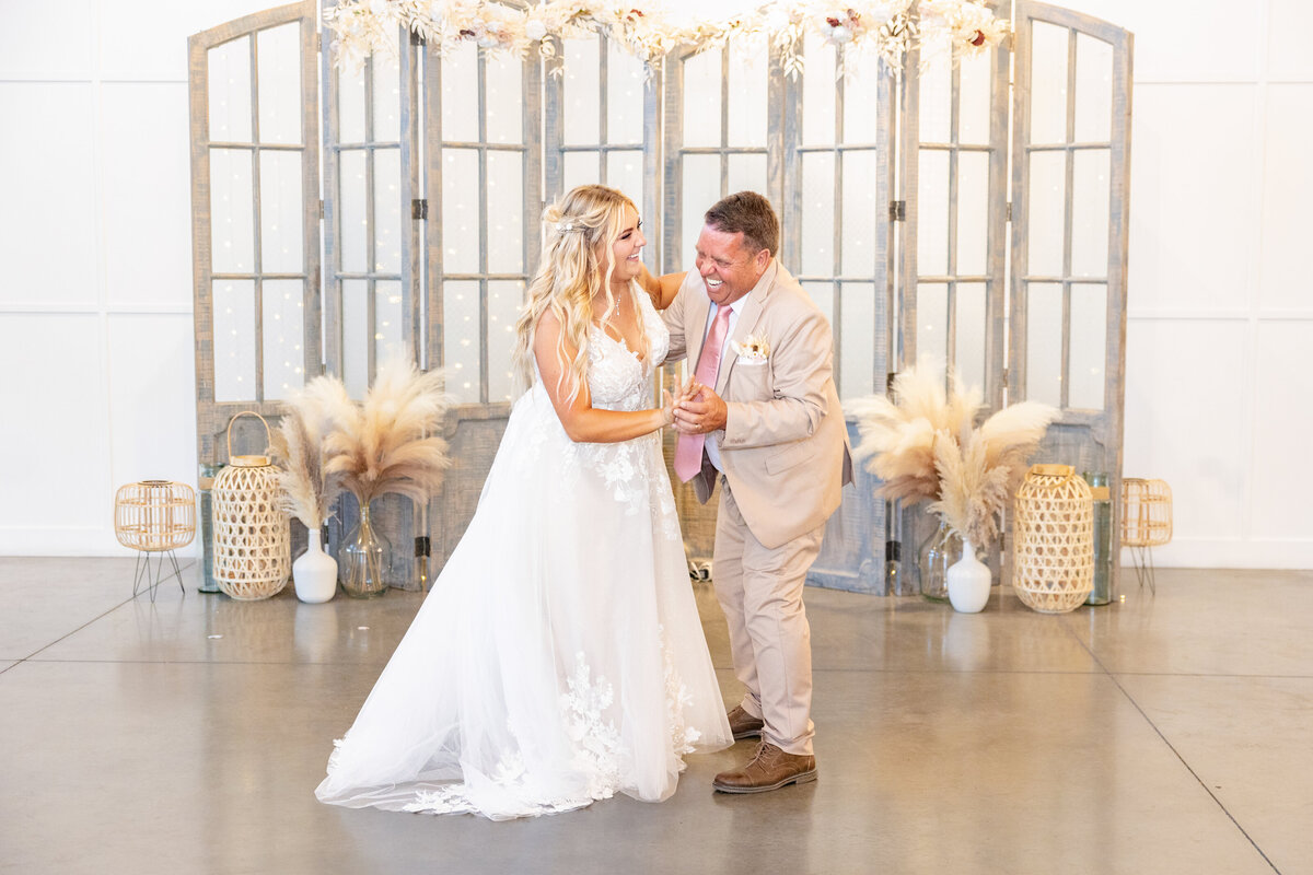 The bride and her father laugh and dance together, celebrating a special wedding moment.